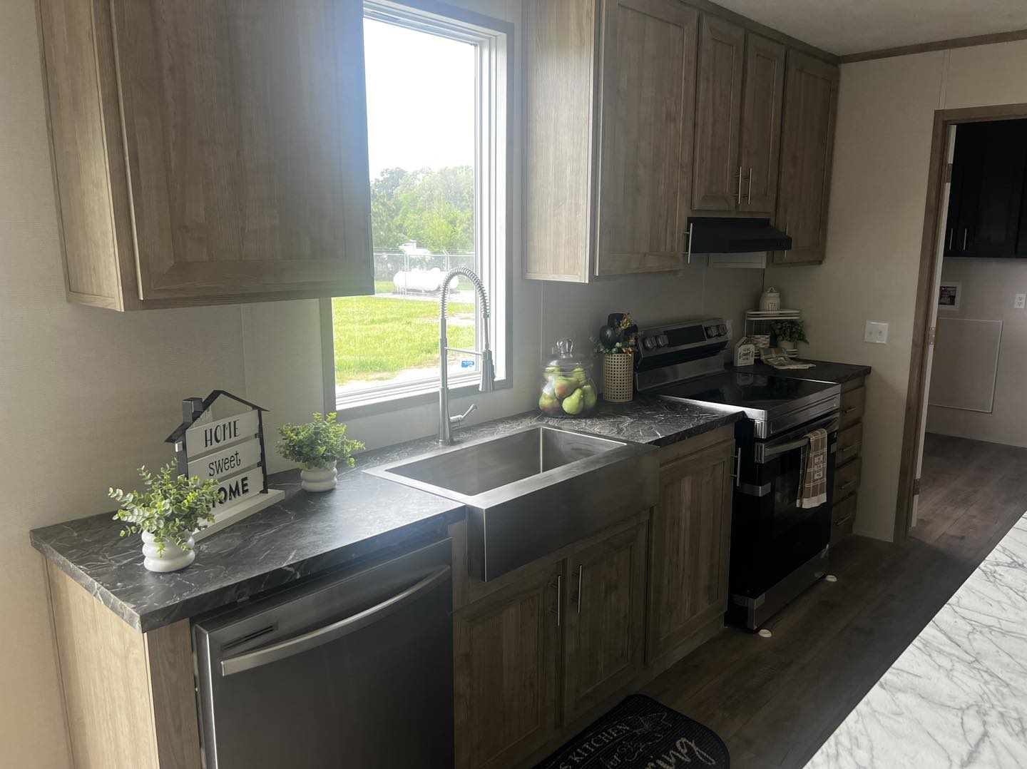 Modern kitchen with wood cabinets, black countertops, and stainless steel appliances. A large window lets in natural light, creating a warm, inviting atmosphere.