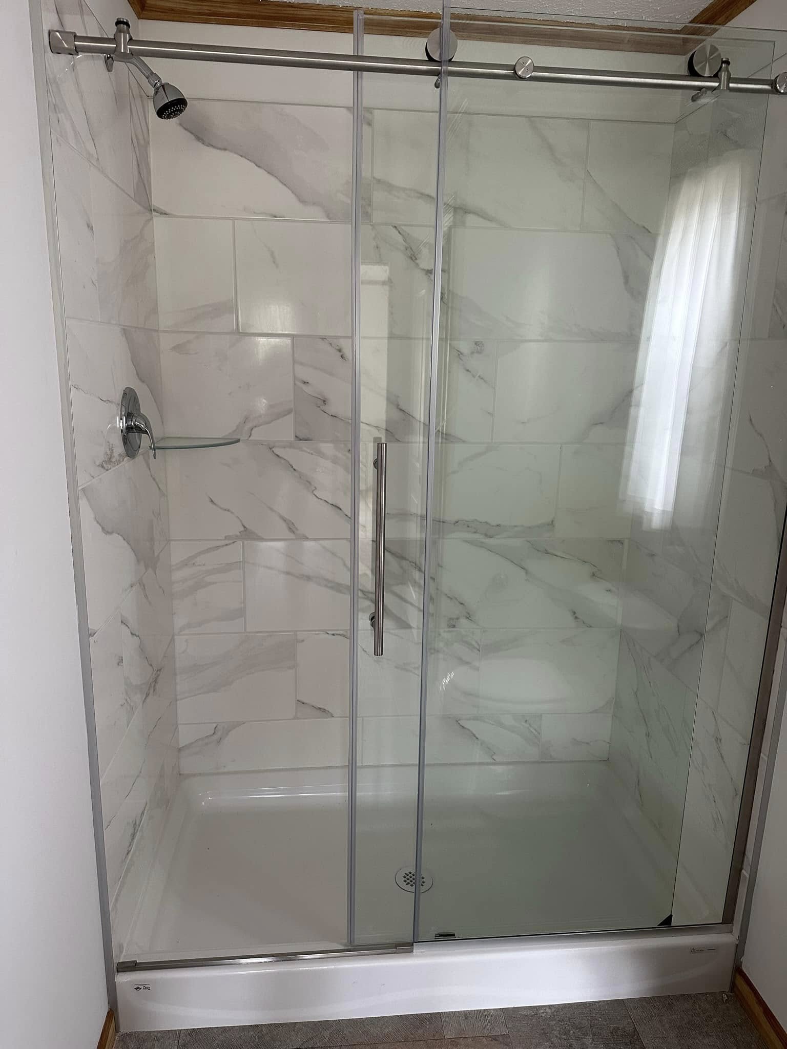 Modern shower with sliding glass doors, chrome fixtures, and elegant white marble tiles. The clean, minimalist design conveys a fresh and serene vibe.
