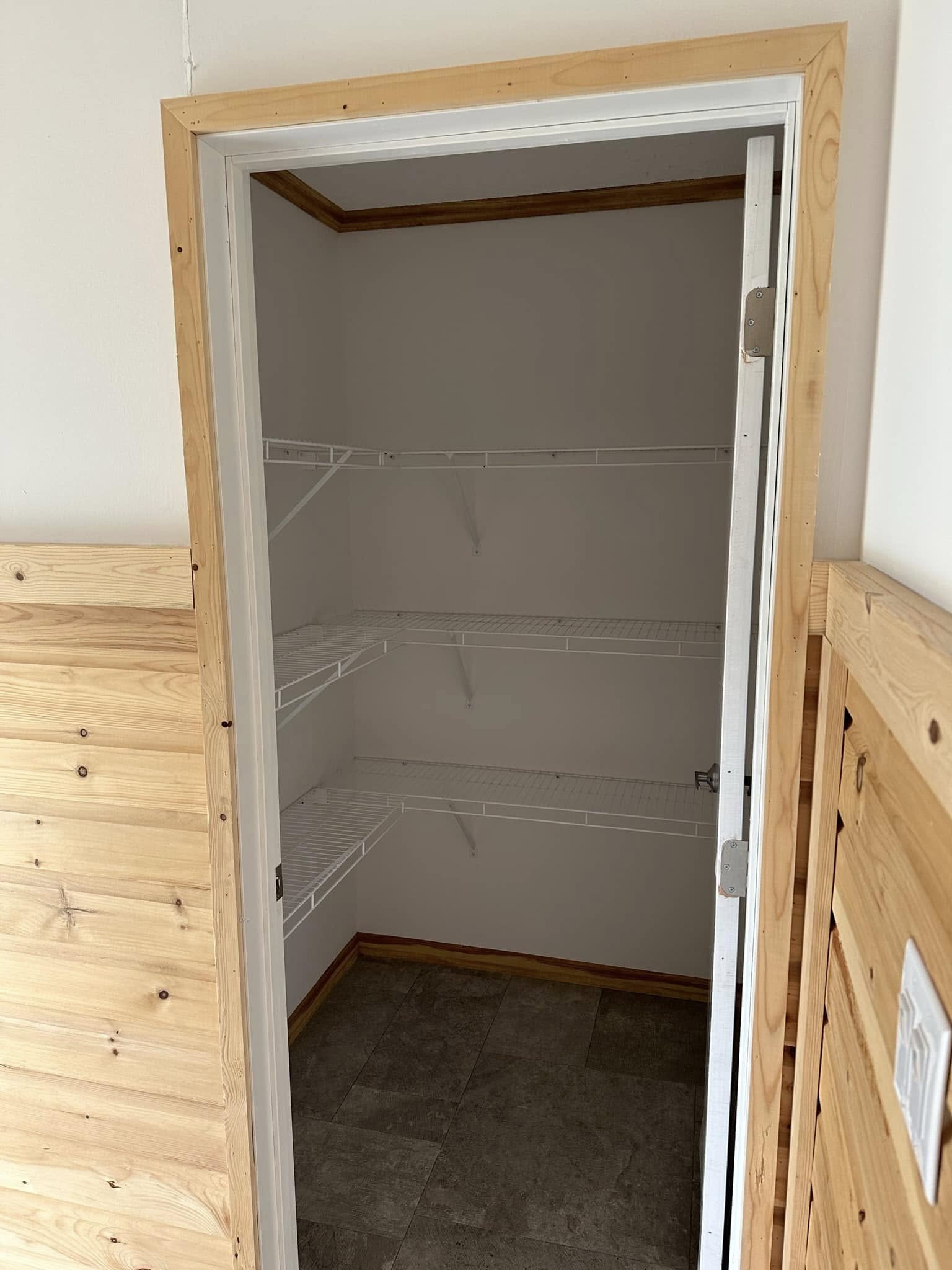Empty pantry with wire shelves, surrounded by wood paneling. The floor is tiled, and the space appears clean and minimalistic, conveying a neutral tone.