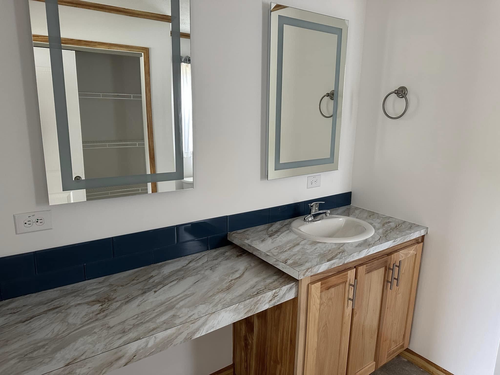 A bathroom vanity features a marble countertop, a white sink, wooden cabinets, and a mirror. Blue tiles add contrast, and a towel ring is on the wall.