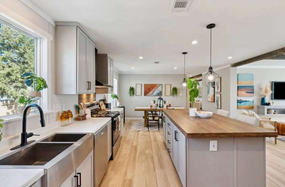 Modern kitchen with light wood floors, a large island with wooden countertop, pendant lights, and stainless steel appliances. Bright and inviting.