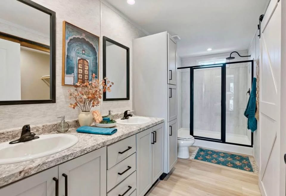 Modern bathroom with double sinks on a marble countertop, framed mirrors, and black fixtures. Features a shower with a glass door and vibrant decor.