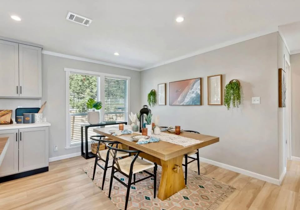 Modern dining room with a wooden table set for four, surrounded by light wood flooring. Neutral tones, plants, and soft lighting create a cozy ambiance.