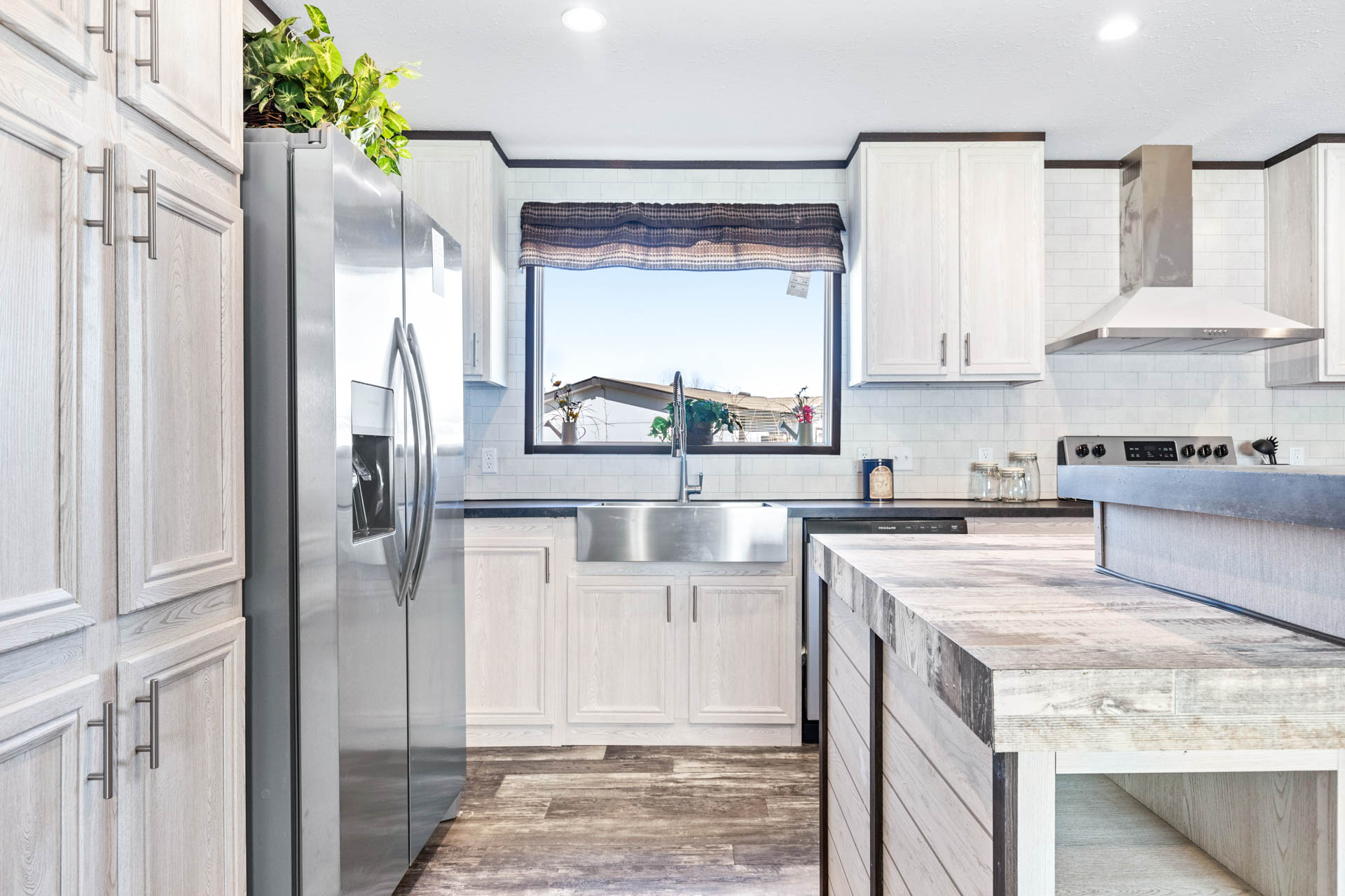 Modern kitchen with light wood cabinets, stainless steel appliances, and a sleek central island. Sunlight streams through a large window, creating a bright and inviting atmosphere.