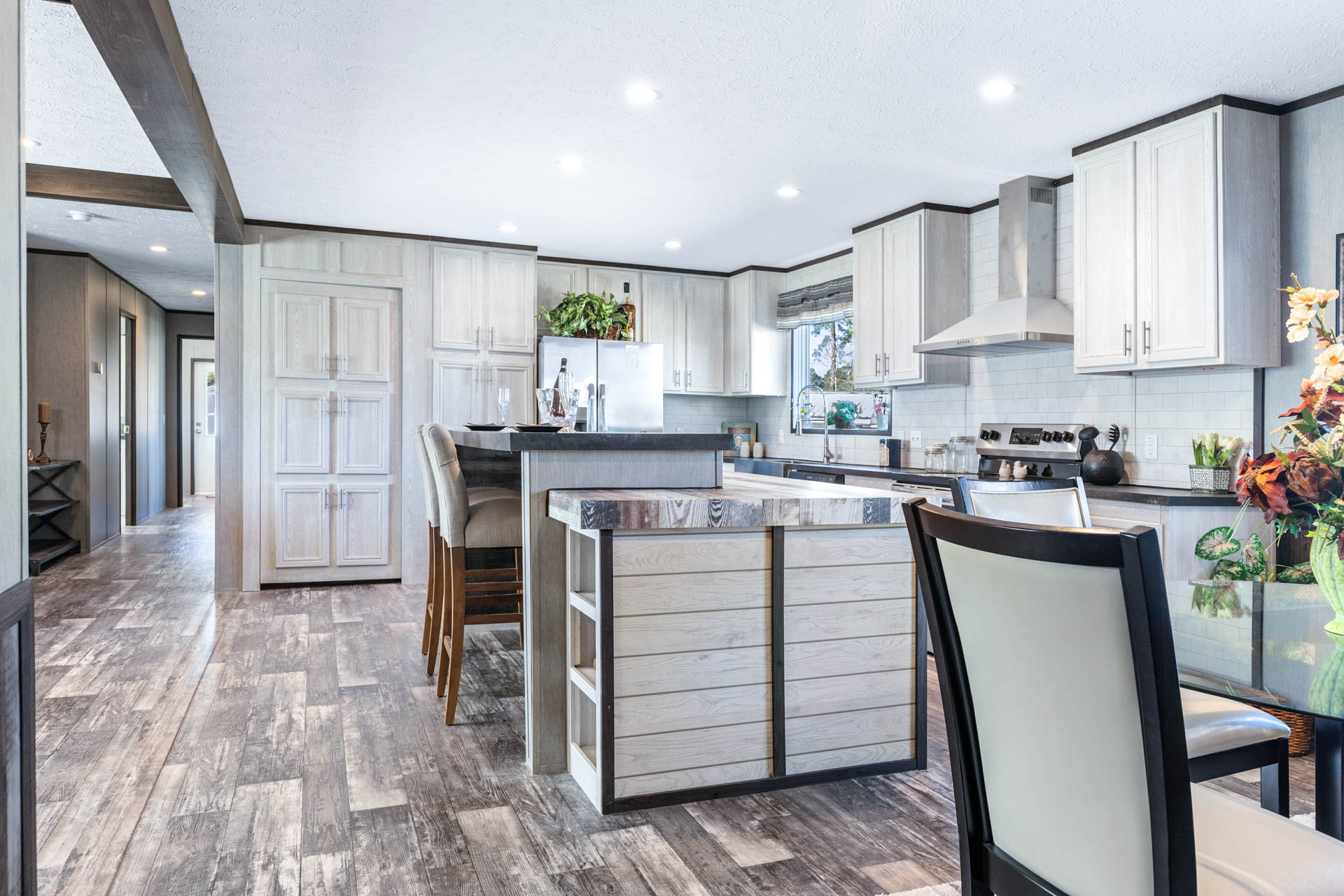 Bright, modern kitchen with white cabinets, dark countertops, and wood flooring. Central island with stools, adjacent dining area with floral decor.