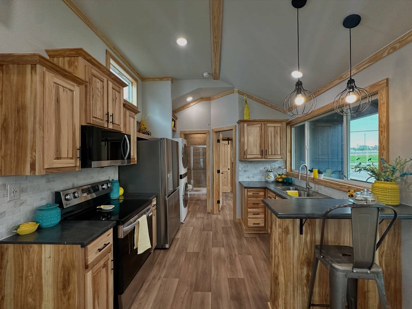 Modern kitchen with wood cabinetry, gray countertops, and stainless steel appliances. Bright yellow and teal accents add warmth and a cheerful vibe.