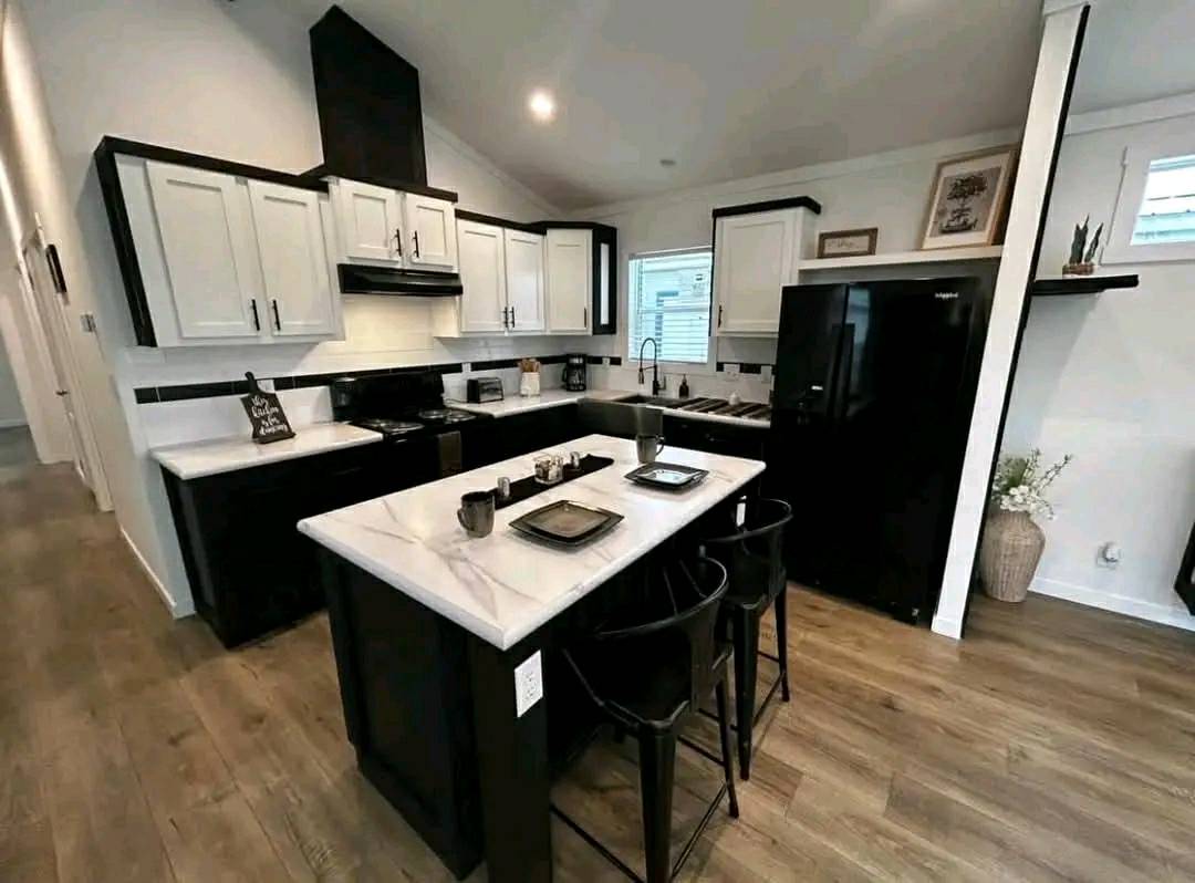 Modern kitchen with white cabinets, black accents, and marble countertops. Central island with barstools, wooden floor, and cozy, welcoming ambiance.