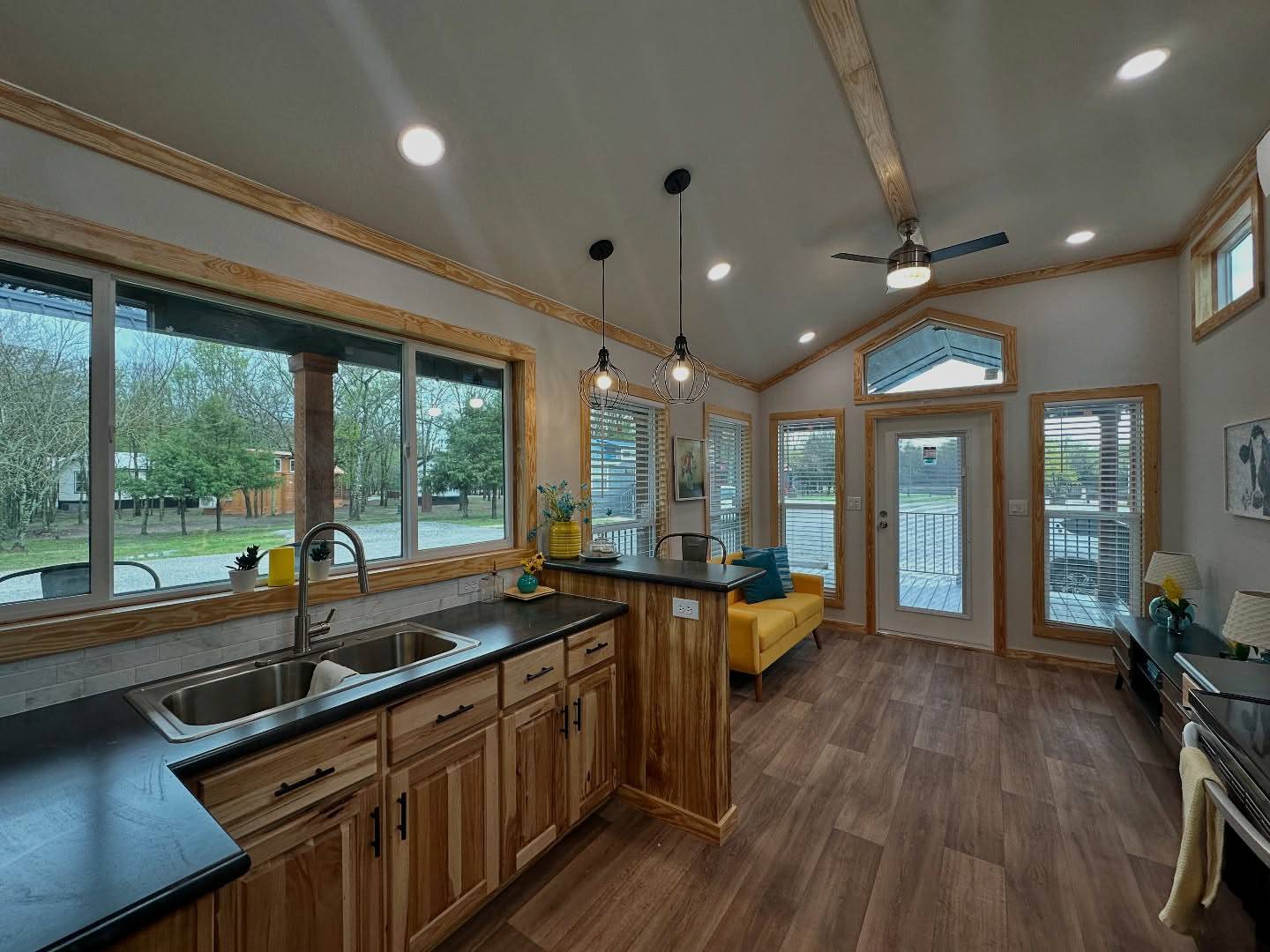 Modern kitchen and living area with wood accents. Large windows offer scenic views. Bright, open space with warm lighting and a cozy atmosphere.