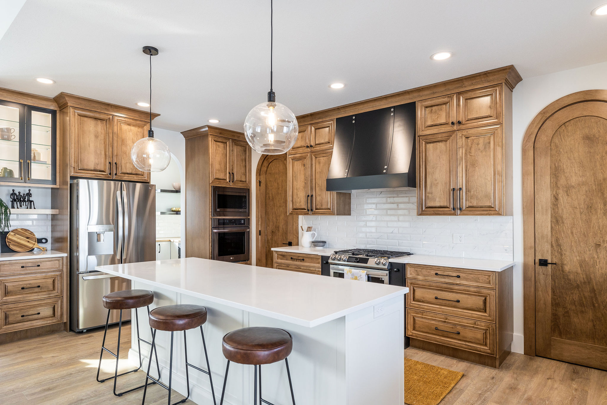Modern kitchen with wooden cabinets, a white island with brown stools, and stainless steel appliances. Pendant lights add warmth and elegance to the space.