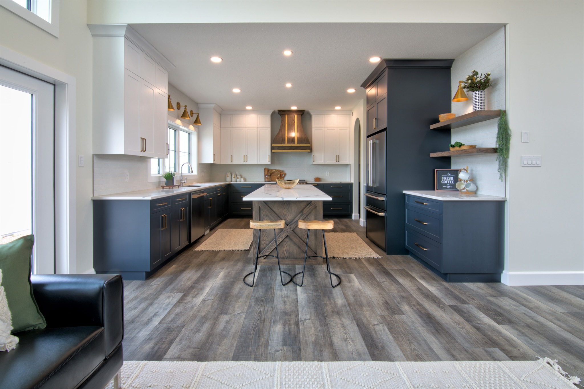 Bright modern kitchen with navy and white cabinetry, wooden floors, and an island with two stools. Warm lighting creates a cozy ambiance.