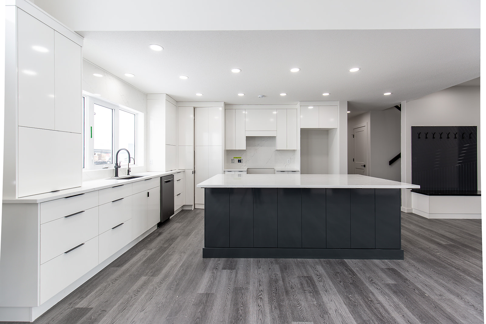 A modern kitchen with sleek white cabinetry, large black island, gray flooring, and ample lighting. The space feels spacious and minimalist.