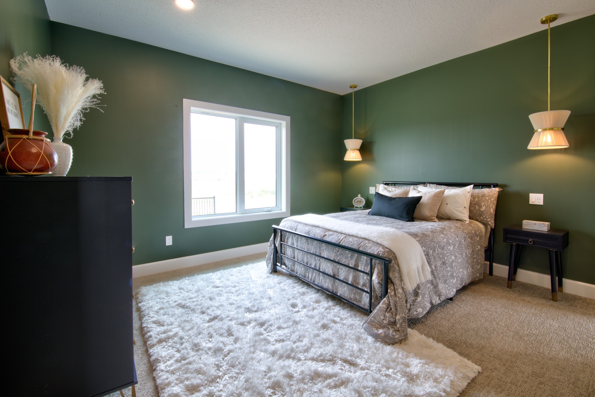 A cozy bedroom features green walls, a bed with neutral bedding, two hanging lamps, and a fluffy rug. Soft lighting creates a warm, inviting atmosphere.
