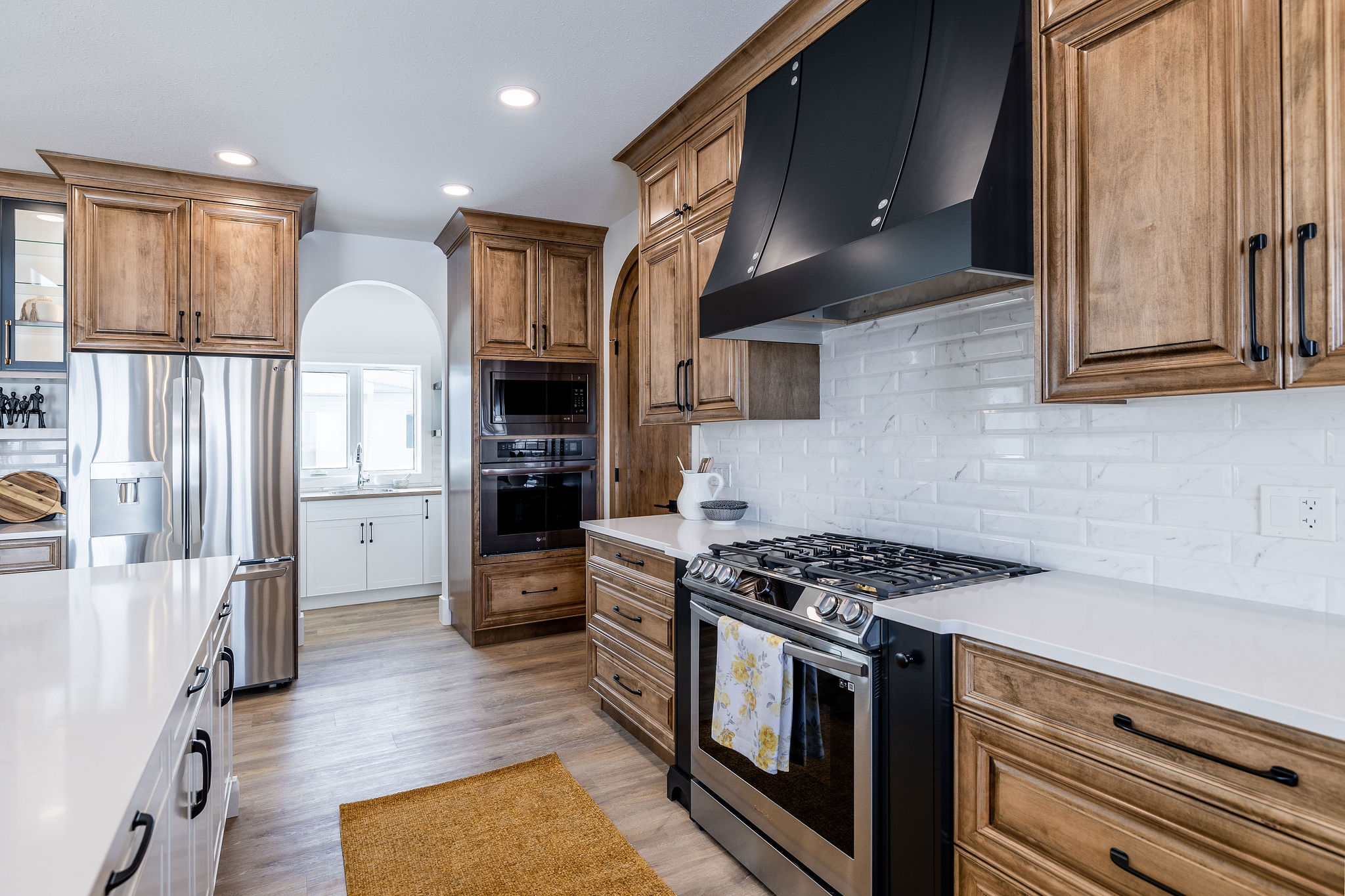 Spacious kitchen with wooden cabinets, stainless steel fridge, and modern appliances. White countertops and backsplash with warm lighting create an inviting atmosphere.