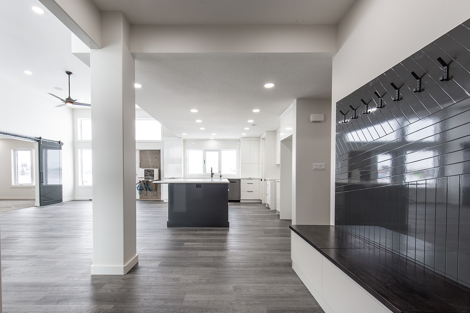 Spacious modern kitchen with white cabinetry, a large island, and dark wood flooring. Bright lighting and a sleek, glossy coat rack add elegance.