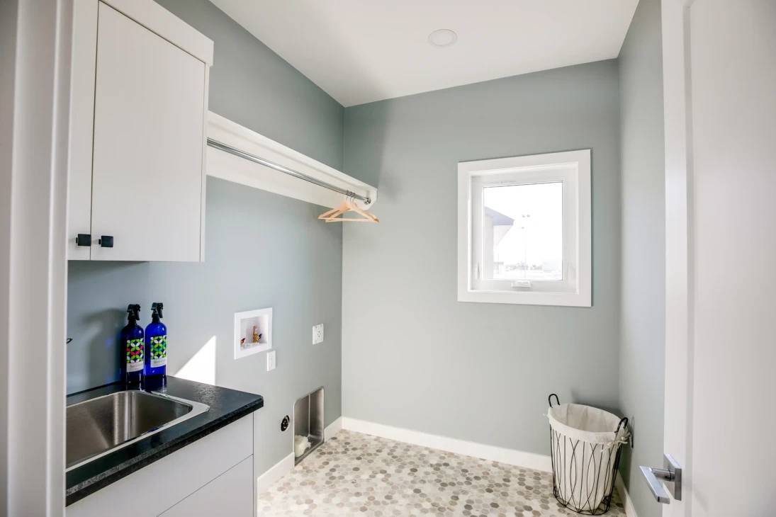 A small laundry room featuring a sink and a window, with light streaming in from the outside.