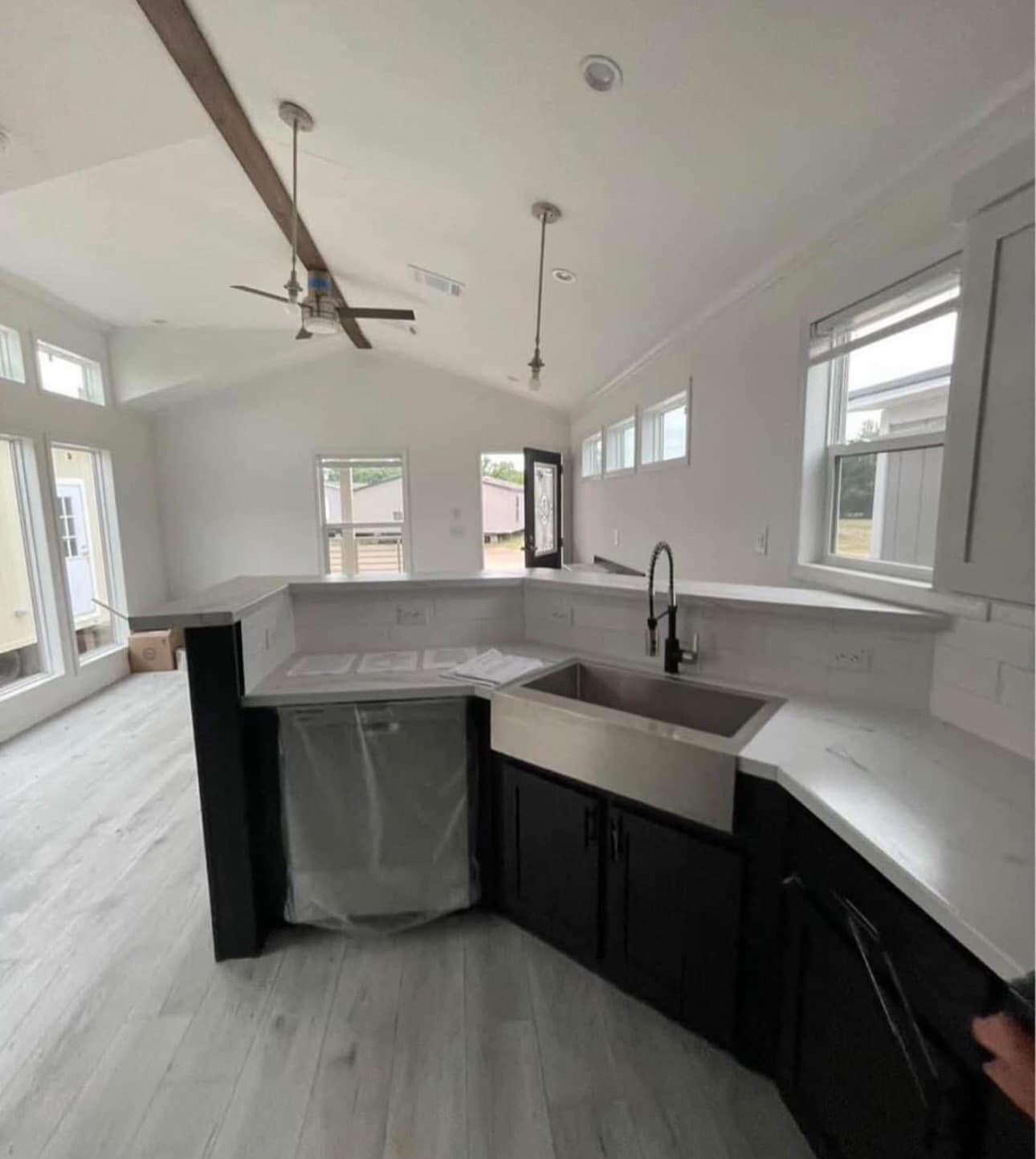 Modern kitchen with a large farmhouse sink, sleek white countertops, and dark cabinetry. Bright natural light streams through multiple windows, creating an airy feel.