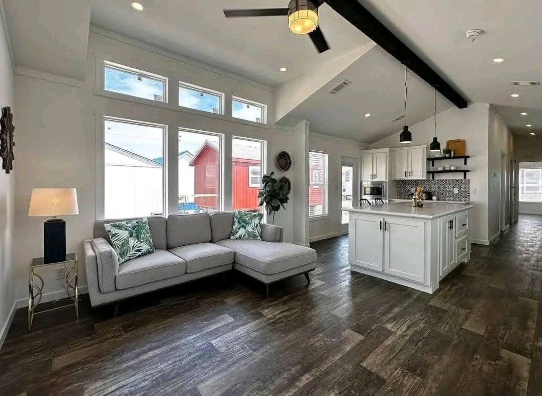 A cozy living room featuring a ceiling fan, with an open view into a modern kitchen area.