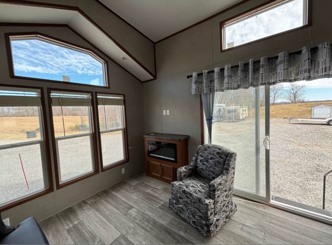 Cozy room with large windows showing a grassy view. Features a patterned armchair, fireplace, and sliding glass door. Bright and inviting atmosphere.