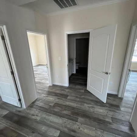 A room with gray wooden flooring, three partially open white doors leading to other rooms, and beige walls, creates a spacious and neutral ambiance.