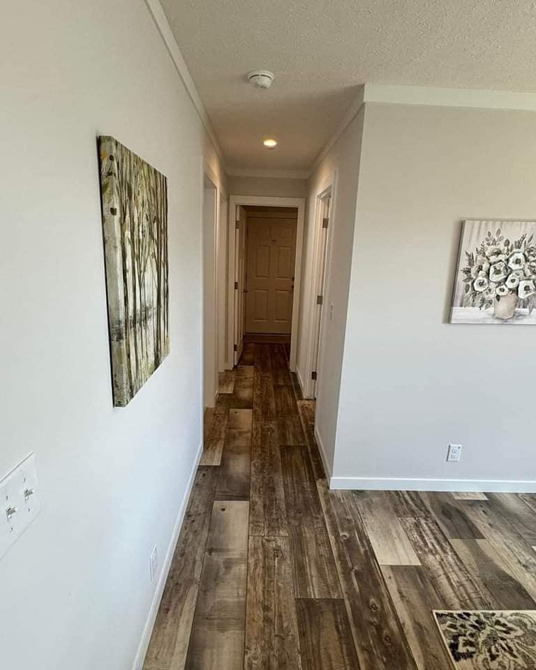 Hallway with light wooden floors and white walls, adorned with nature paintings. It leads to a closed door, evoking a calm, orderly ambiance.