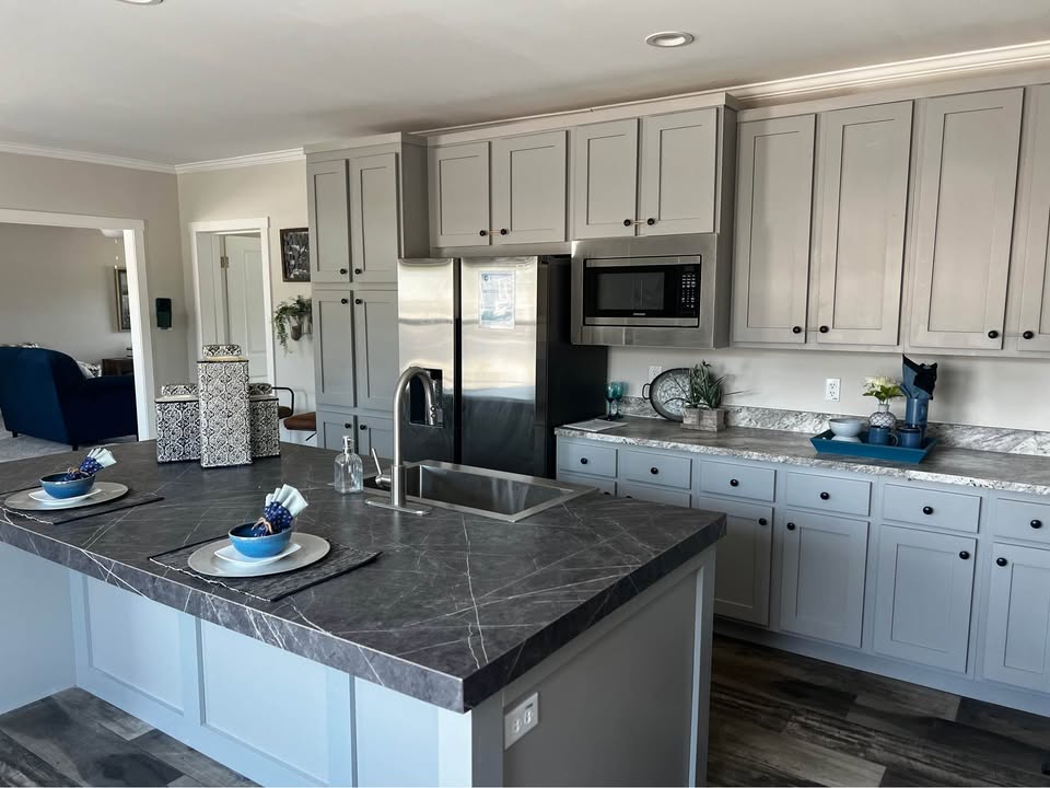 Modern kitchen with gray cabinets, marble countertops, and a central island with two place settings. Stainless steel appliances and a sleek, clean design.