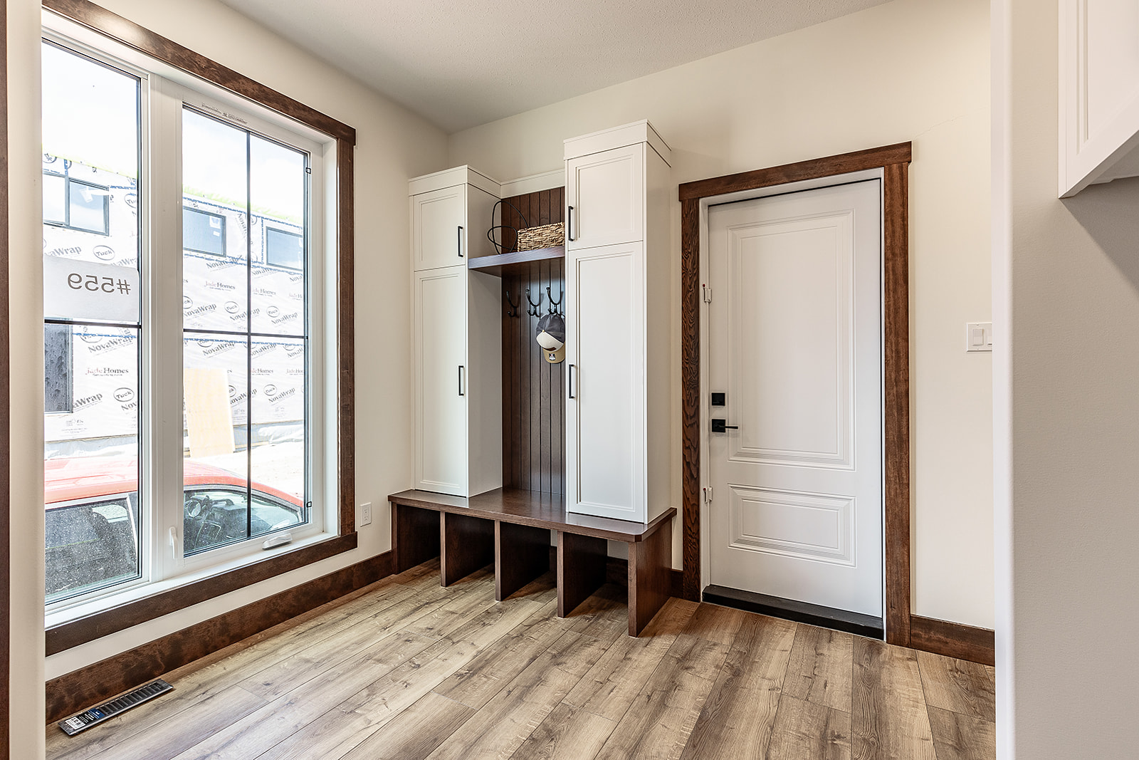 Modern mudroom with a white door, wood-trimmed cubbies, and hooks. Tall cabinets flank the bench. Sunlight streams in through large windows, creating a warm, inviting atmosphere.