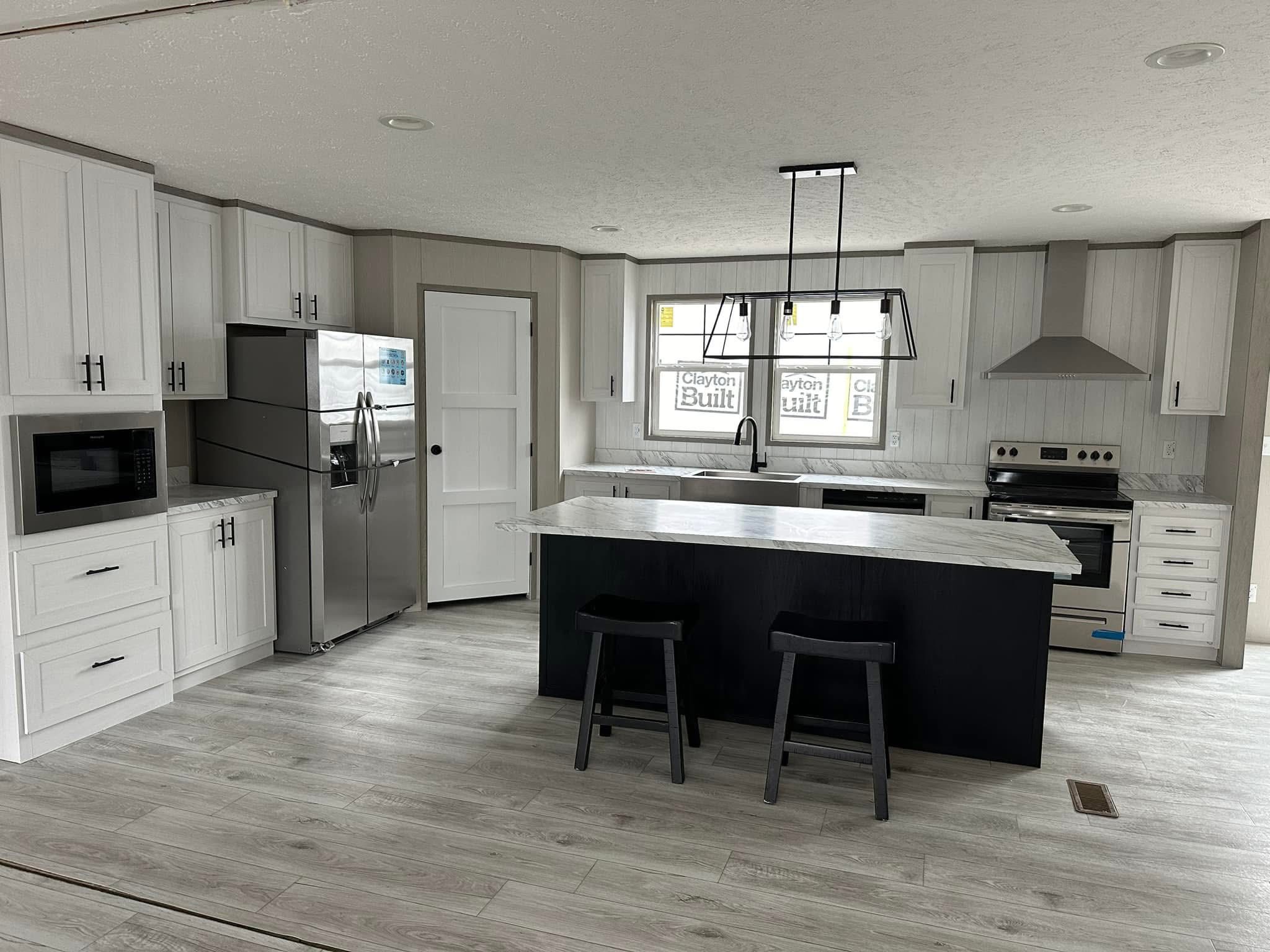 Modern kitchen with white cabinets, stainless steel appliances, and a large island with two black stools. Bright, clean, and contemporary.