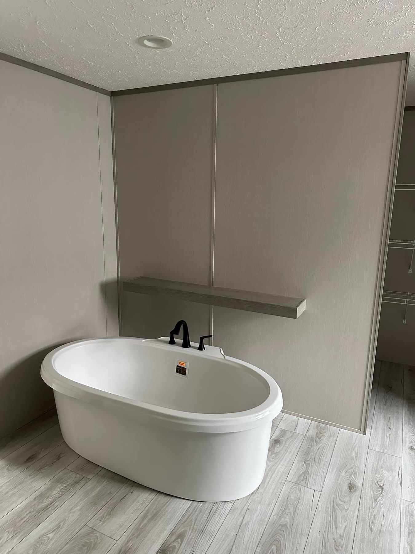 Minimalist bathroom with a freestanding white oval bathtub on light wood flooring. Neutral walls create a calming ambiance. Wall shelf above the tub.