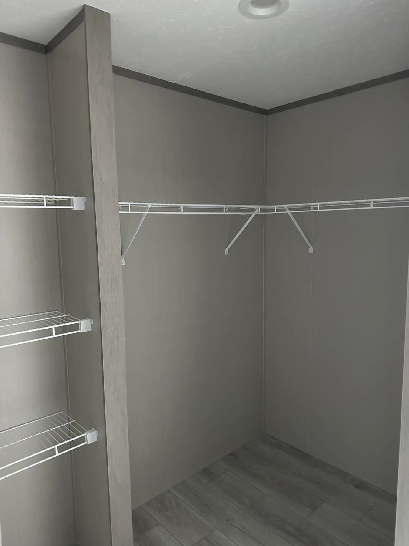 Minimalist gray walk-in closet with open wire shelving on the left and angled racks on the right. The space is empty, conveying a clean, organized feel.