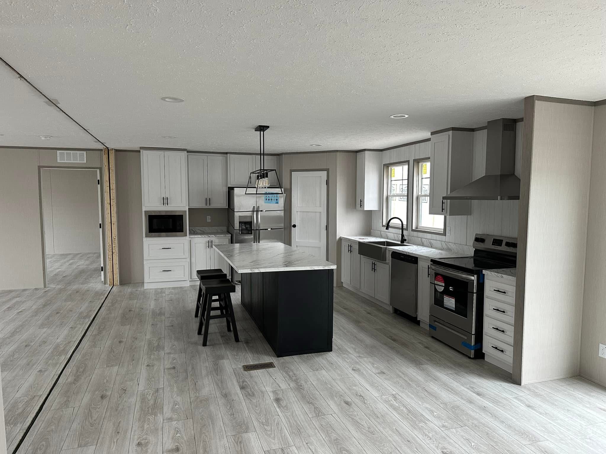 Modern kitchen with light wood flooring, white cabinets, and a large island with dark base. Stainless steel appliances give a sleek, clean look.