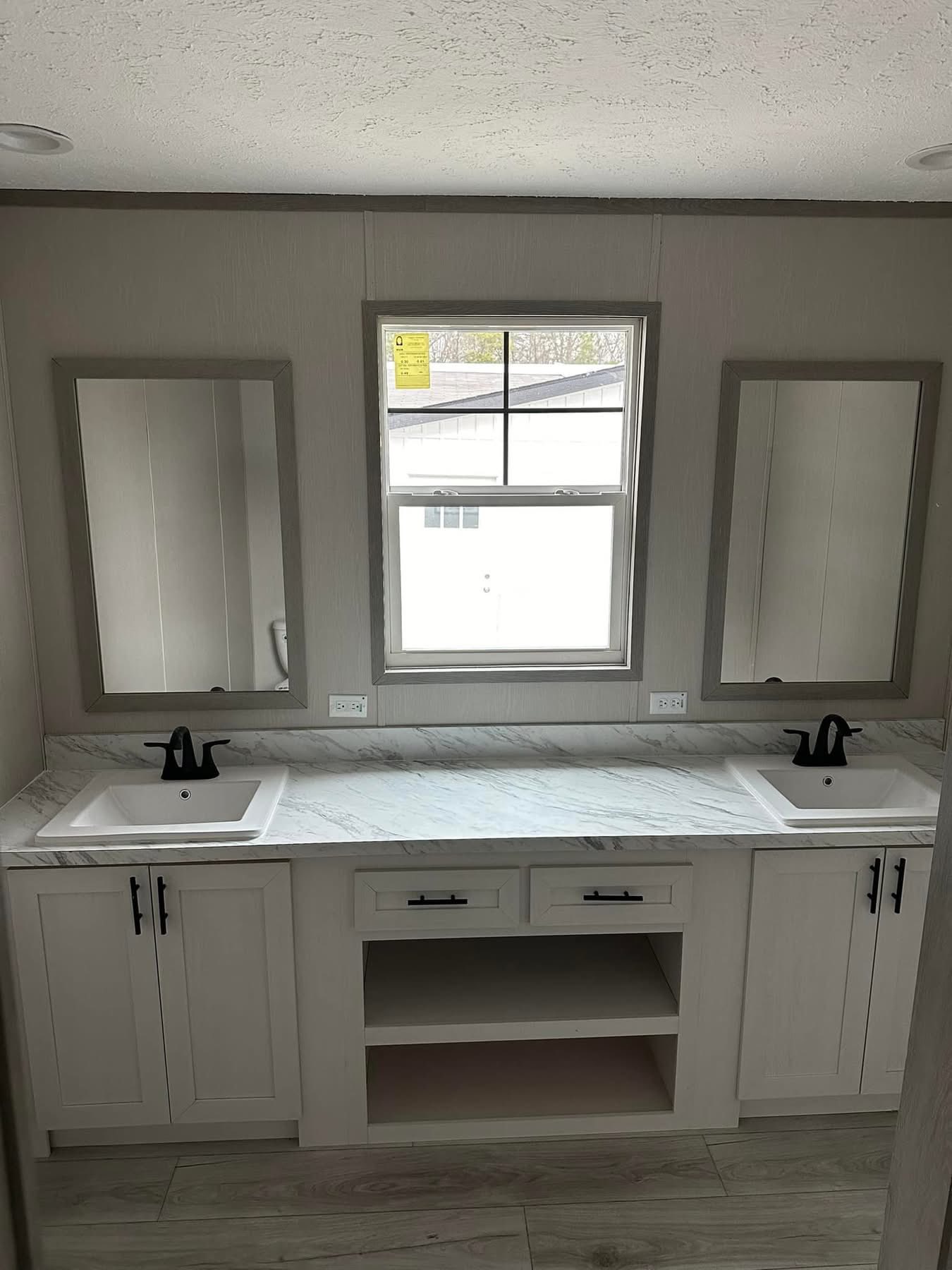 Modern bathroom with two white sinks, black faucets, and a marble countertop. Two mirrors flank a central window, creating a clean, bright ambiance.