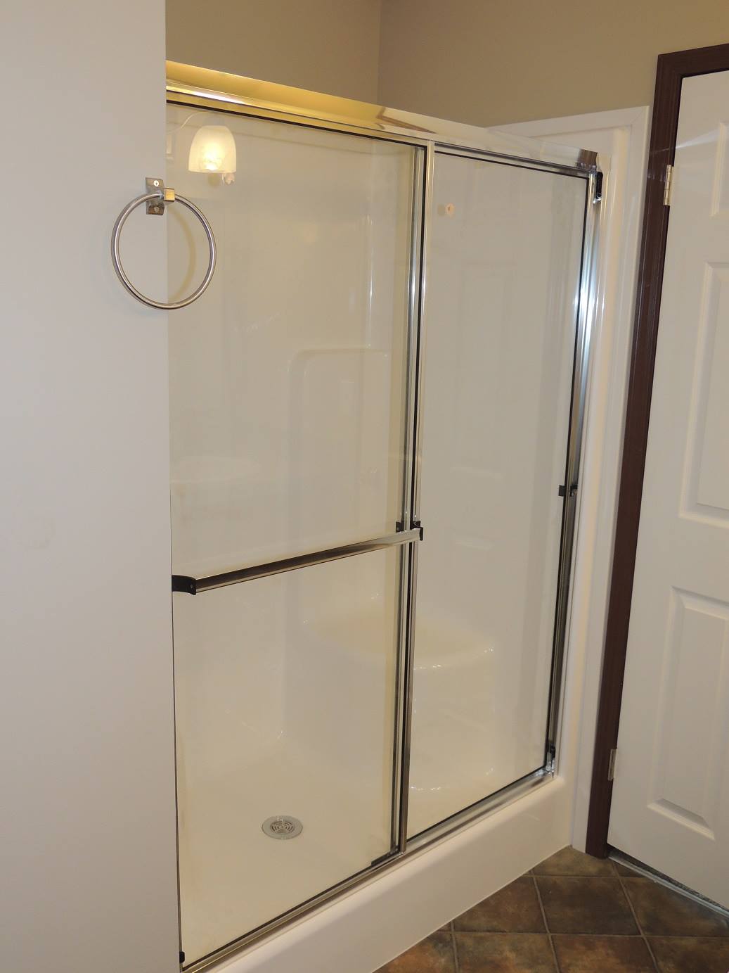 Shower area with glass sliding doors and chrome frame, set in a tiled bathroom. A towel ring is adjacent, reflecting a clean, minimalistic design.