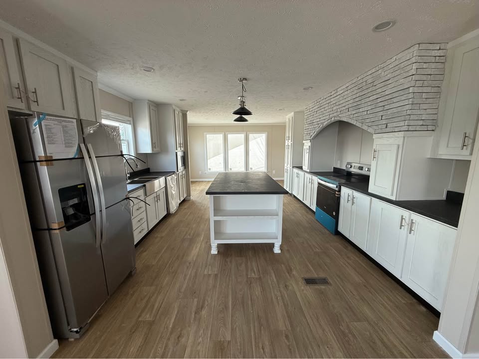 Spacious kitchen with white cabinets, stainless steel appliances, and a black countertop island. Light wood flooring and brick accent wall add warmth.