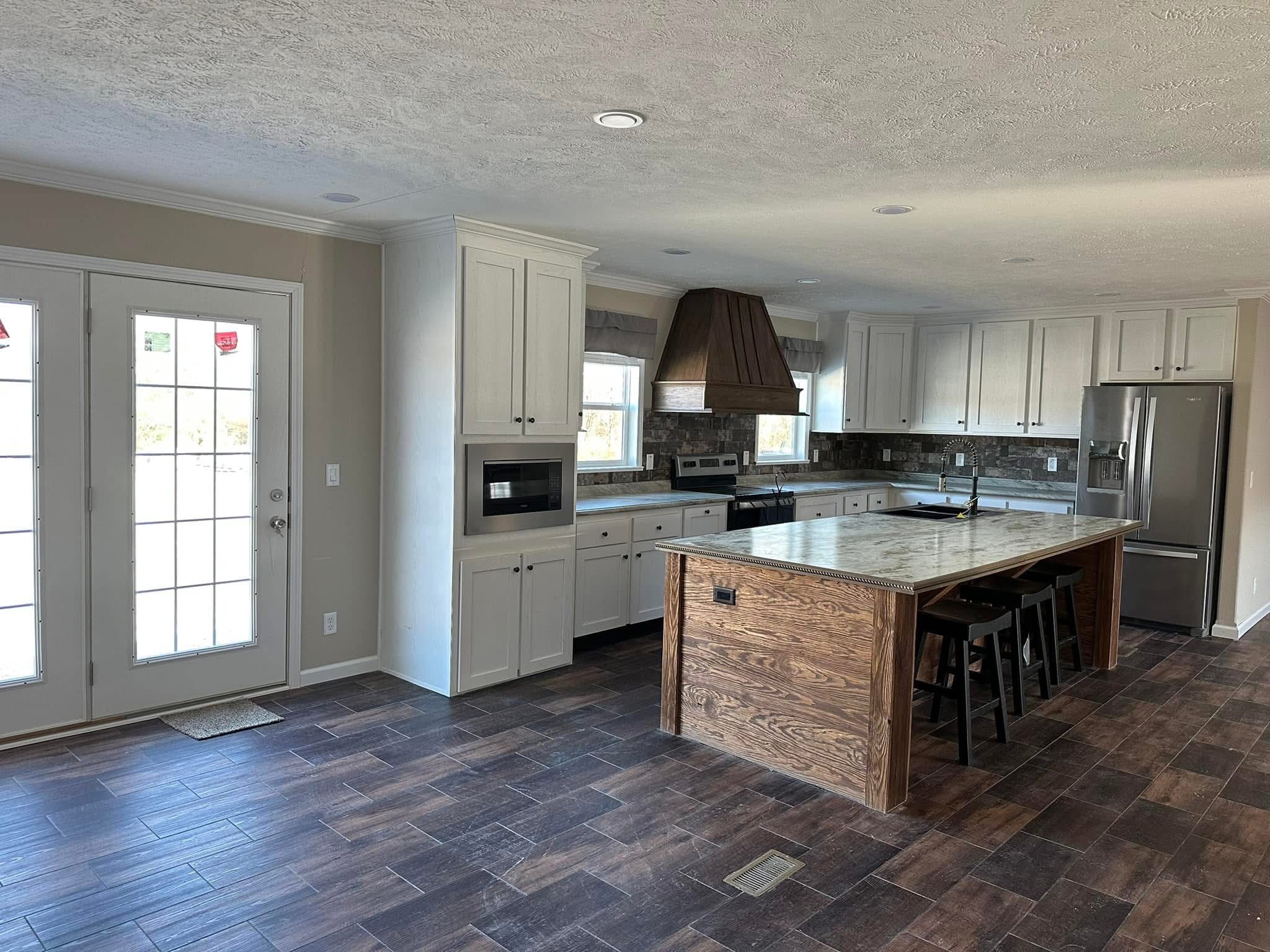 Spacious kitchen with dark wood floor, a large island with stools, white cabinets, stainless steel appliances, and double glass doors. Warm, inviting ambiance.