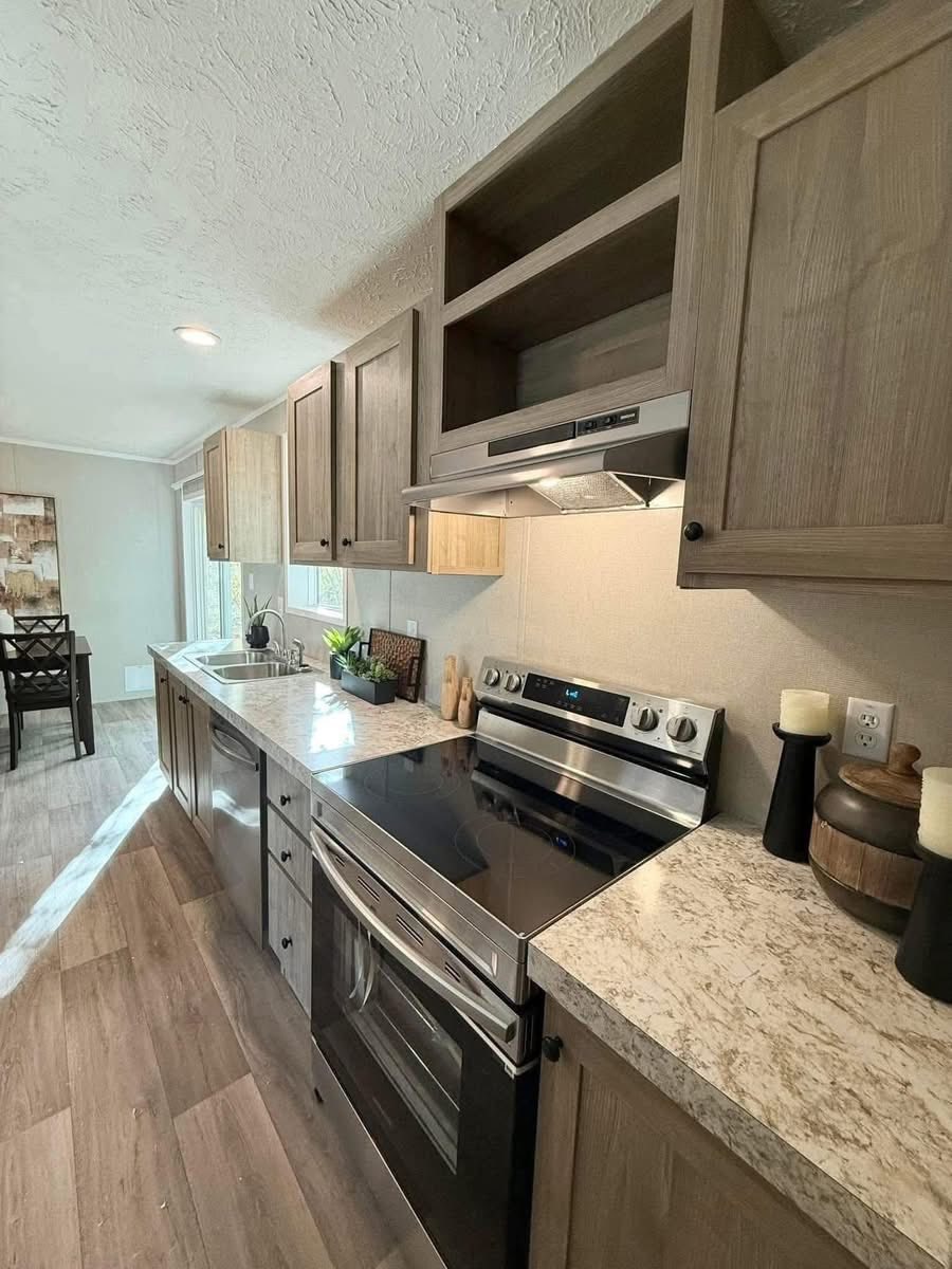 Modern kitchen with light wood cabinets, marbled countertops, and stainless steel appliances. Bright atmosphere with natural light and dining area visible.