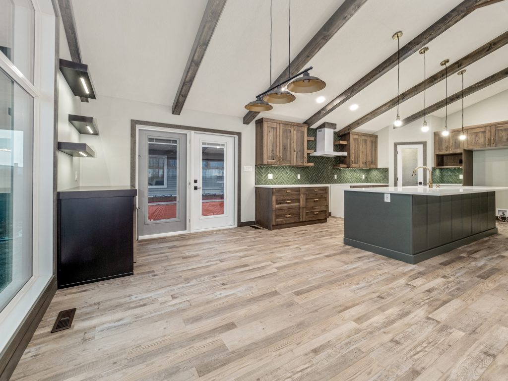Spacious kitchen with rustic charm, featuring exposed wooden beams, hardwood floors, and modern pendant lighting. Warm tones and green tile backsplash enhance coziness.