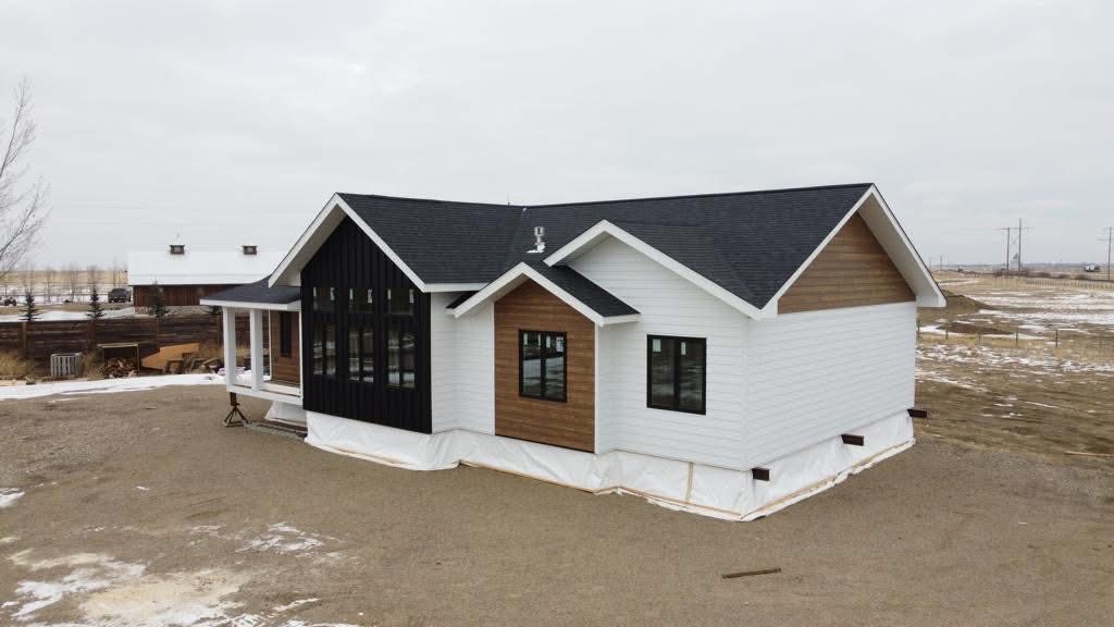 A modern house with white and dark wood siding and a black roof sits on a snowy, barren landscape under a cloudy sky, evoking a serene, minimalist vibe.
