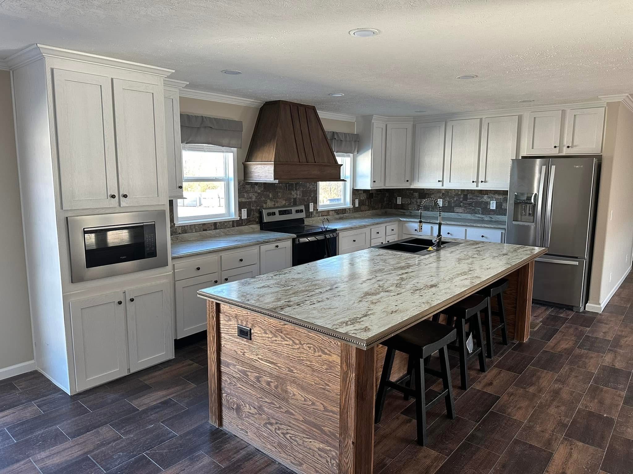 Spacious kitchen with white cabinets, large wood island, and dark stone backsplash. Modern appliances and bar stools create a warm, inviting atmosphere.