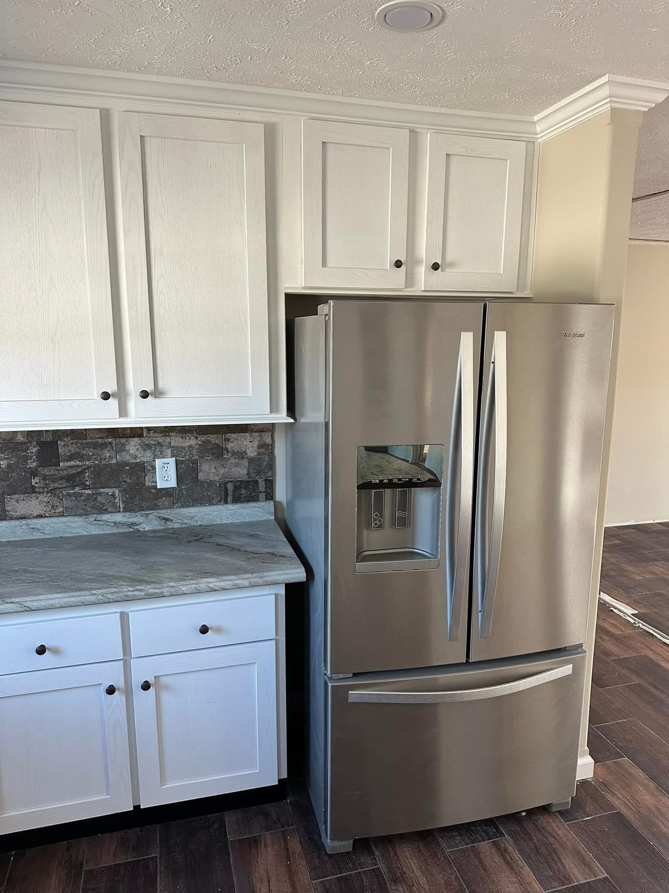Modern kitchen with stainless steel French door fridge, white cabinets, and stone tile backsplash. Neutral tones and sleek design create a clean, stylish look.