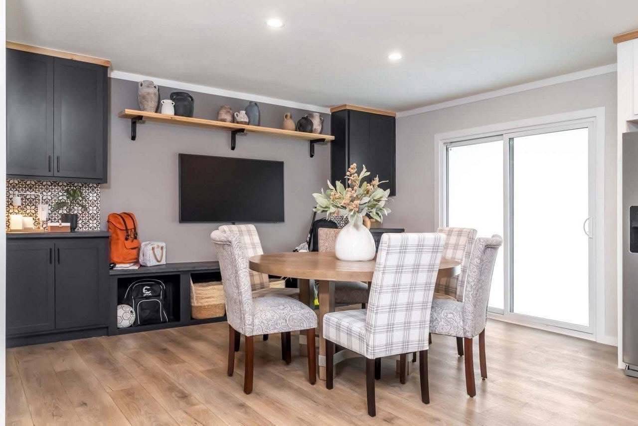 A modern dining room features a round wooden table with six plaid chairs. Black cabinets and shelves with decorative vases enhance the cozy ambiance.