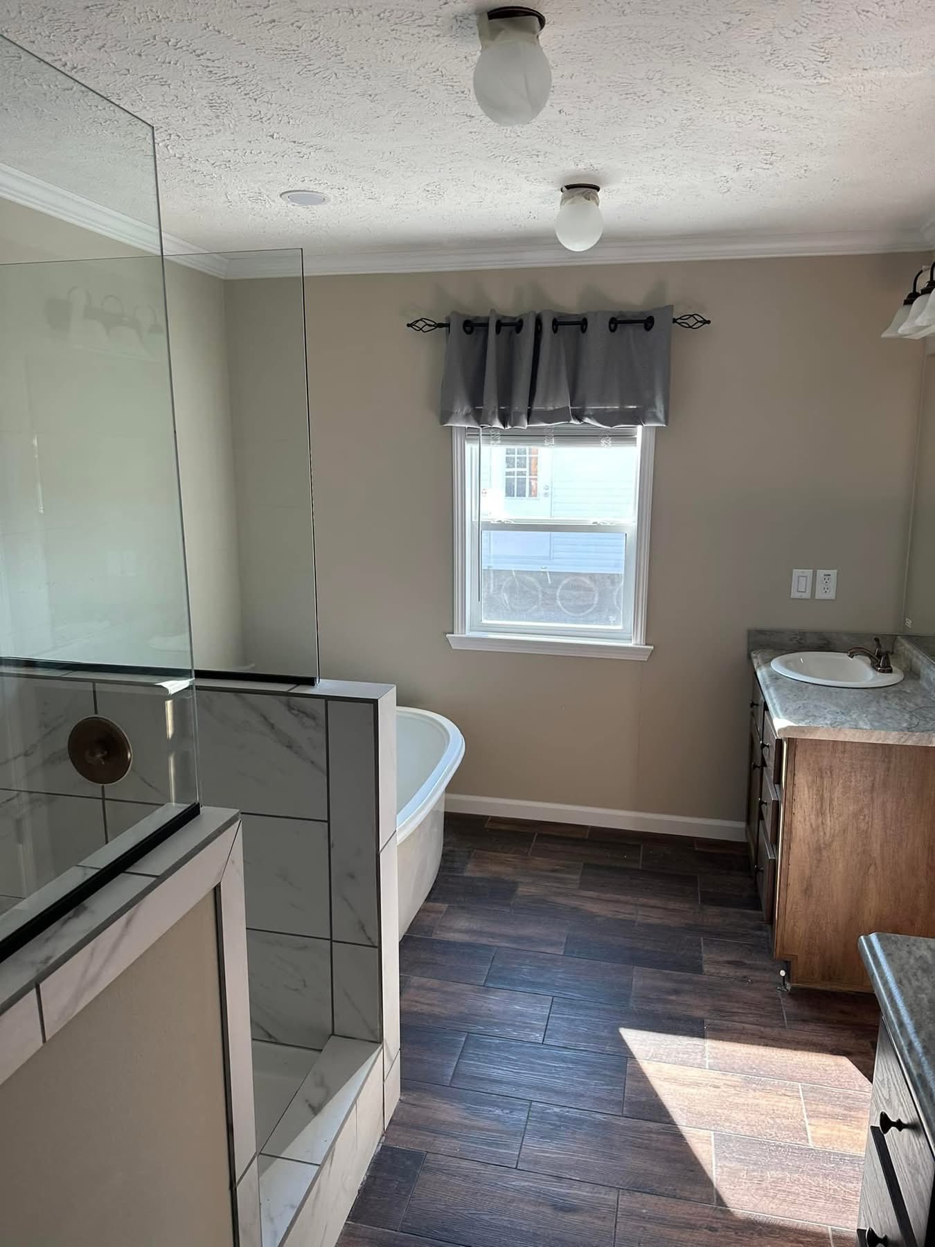 Modern bathroom with neutral tones, featuring a glass shower, freestanding tub, single vanity with marble countertop, and wood-look tile flooring.