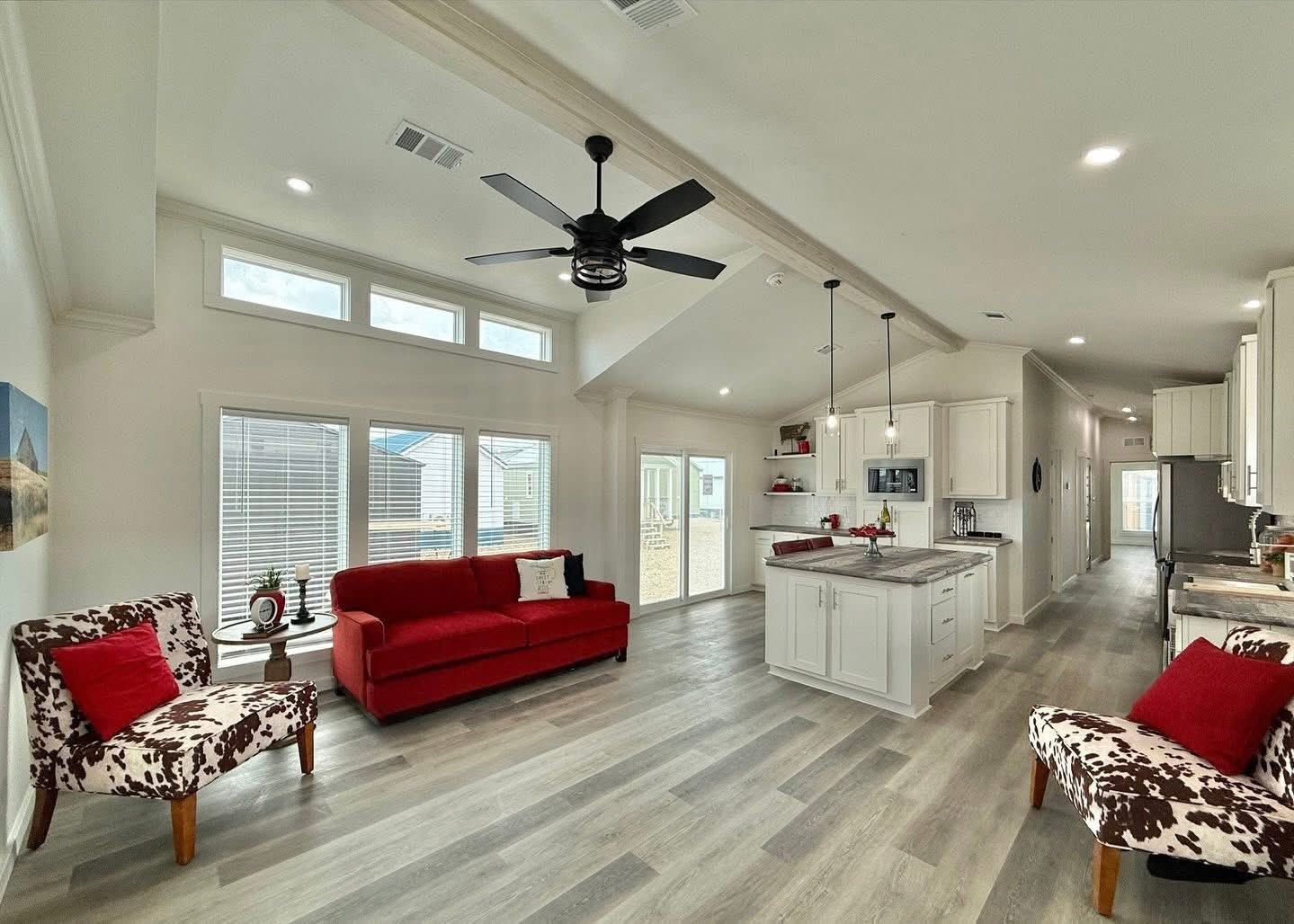 Spacious living room and kitchen with vaulted ceilings. Red sofa and cow-print chairs add vibrant contrast. Bright and airy with modern decor.