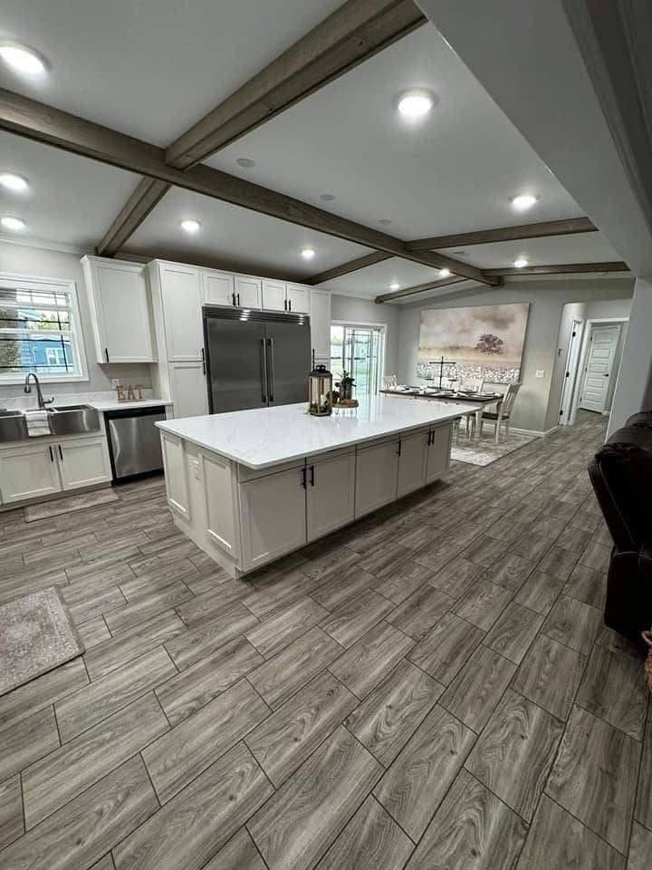Modern kitchen with white cabinets, marble island, and stainless steel appliances. Wood beams and gray-toned laminate flooring create a warm ambiance.