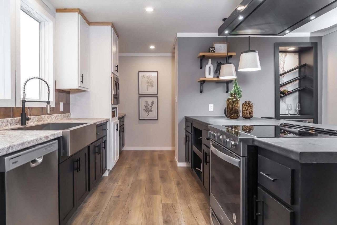Modern kitchen with black and white cabinets, stainless steel appliances, and wood flooring. Stylish decor includes pendant lights and wall art.