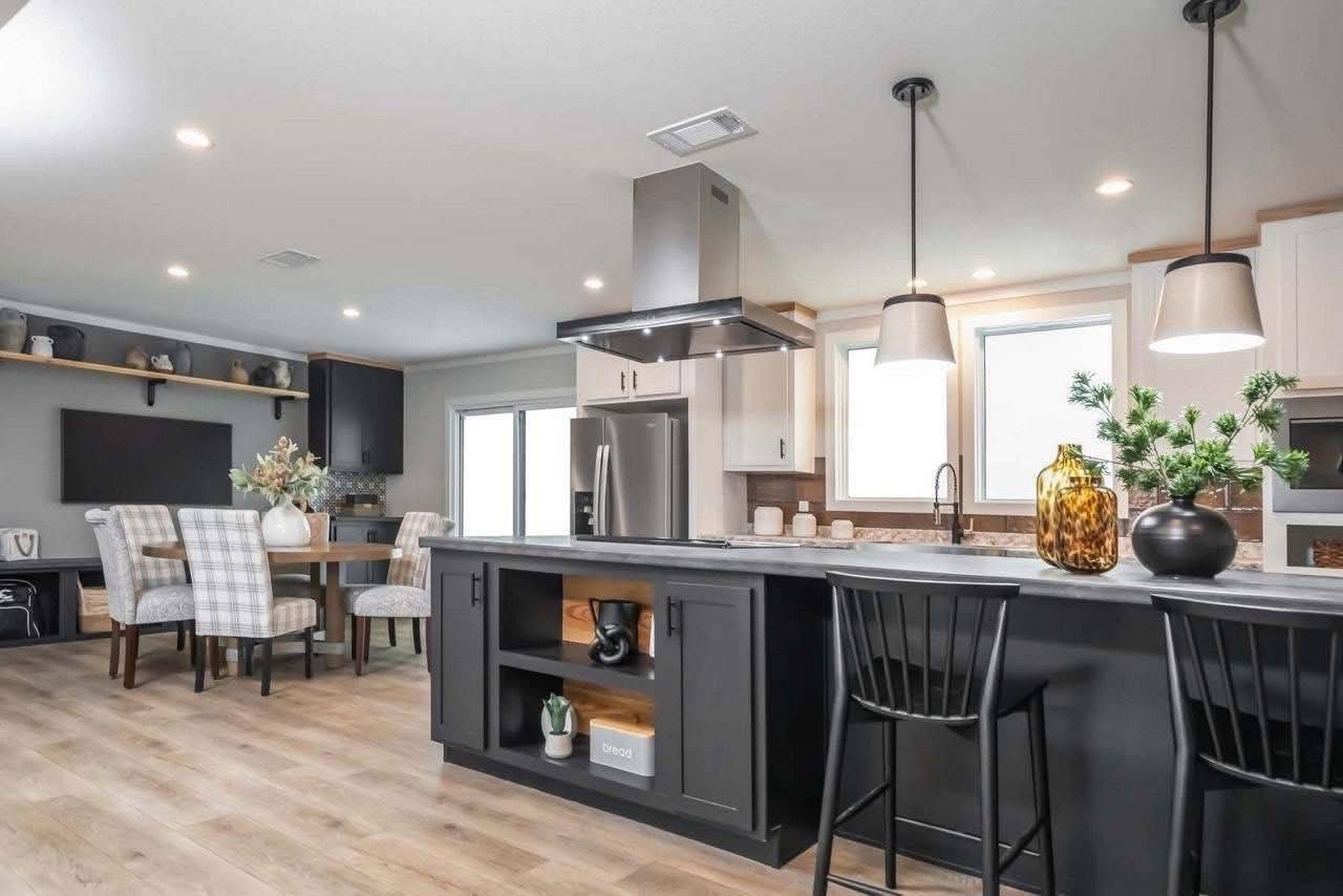 Modern kitchen and dining area featuring a sleek black island with chairs, pendant lights, neutral cabinets, plants, and a cozy dining table with plaid chairs.