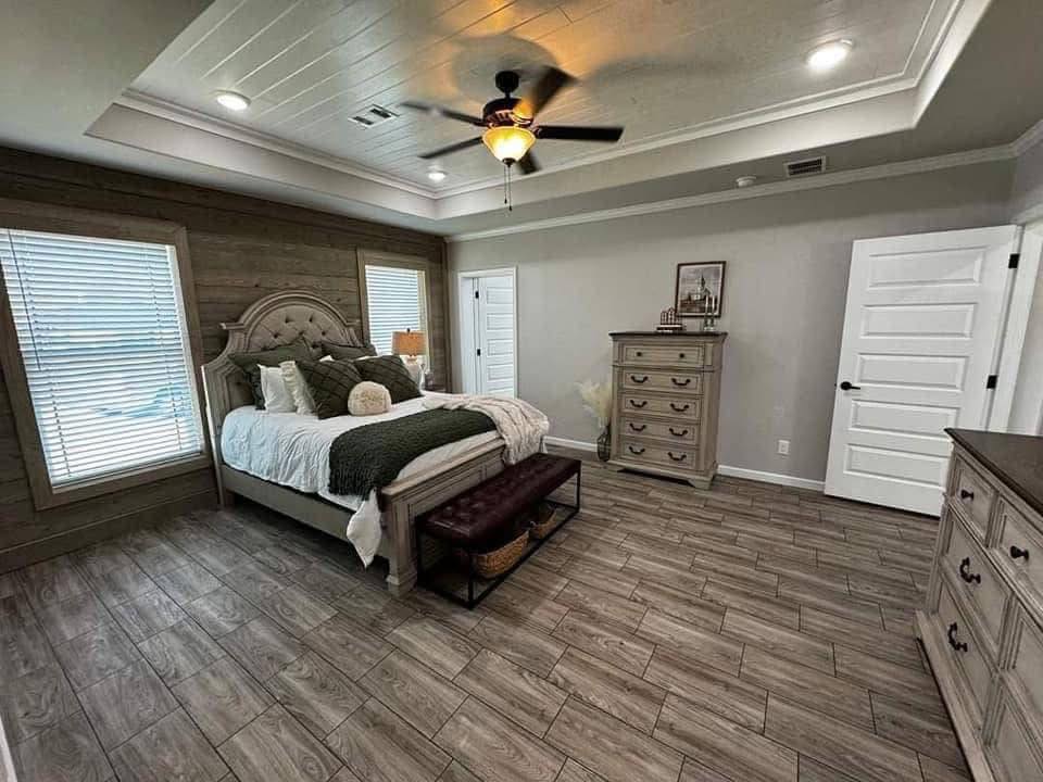 Cozy bedroom with a large, tufted bed, green accents, and wood panel walls. A ceiling fan, stylish dresser, and bench add warmth and elegance. Calm tone.