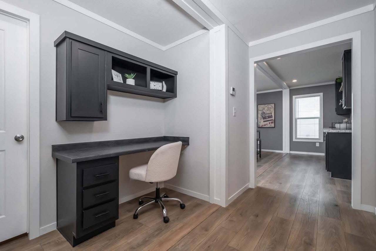 Modern home office nook with a sleek black desk and shelving, an off-white swivel chair, and light wood flooring. The adjoining room is visible in the background.