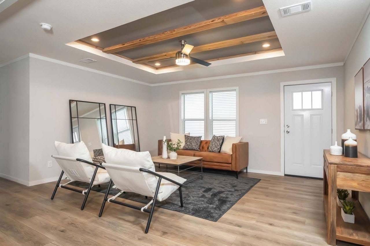 Modern living room with a cozy brown leather sofa, two white chairs, and a wooden ceiling with recessed lighting. A gray rug and large mirrors add elegance.