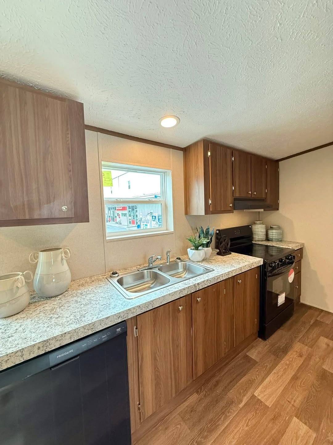 A modern kitchen with wood cabinets, marble countertops, and stainless steel sink. Cozy and inviting with soft lighting and decorative plants.