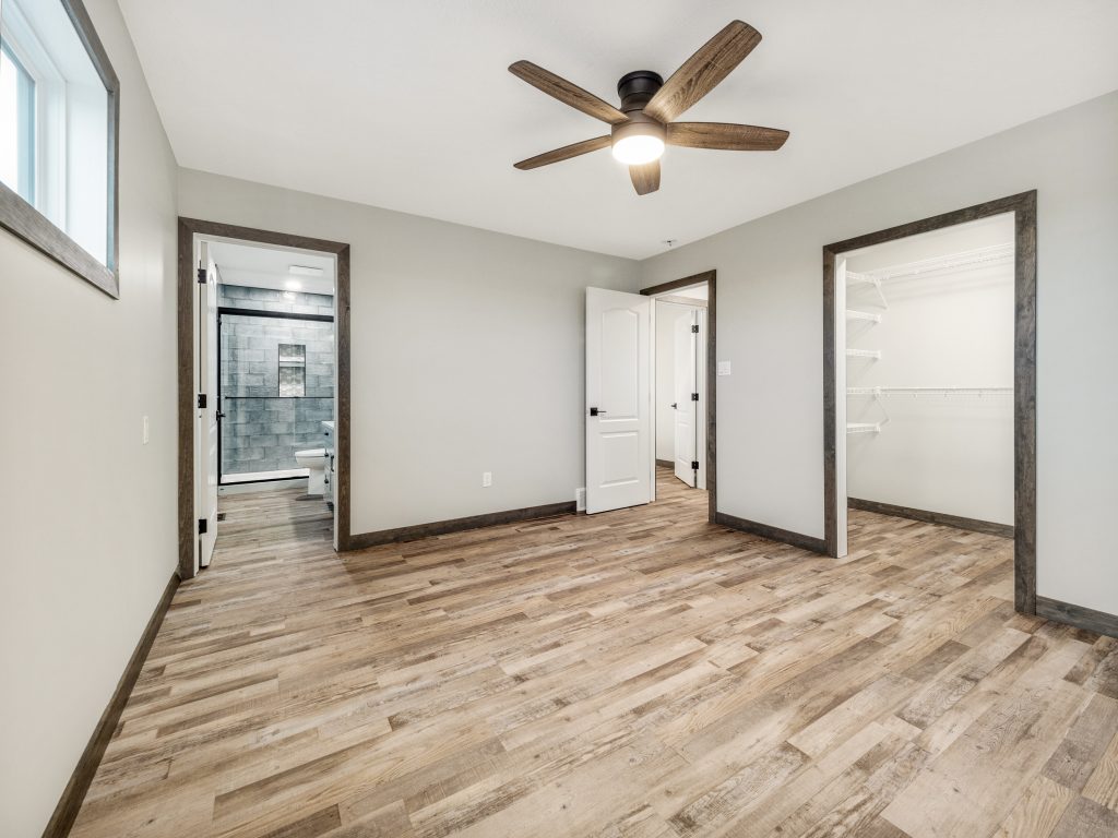 A minimalist office space with a large wooden desk, gray cabinets, and shelves. A window at the center overlooks trees, and light wooden flooring adds warmth.